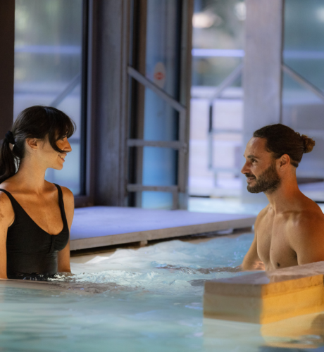 Due persone sorridenti si rilassano in una piscina termale illuminata.
