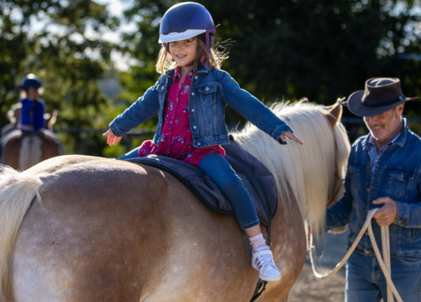 Bambina felice a cavallo, guidata da un uomo sorridente in un giorno soleggiato.